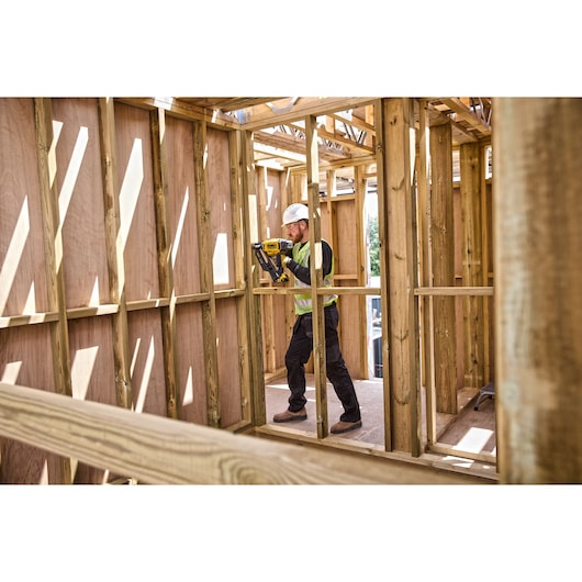 Person using a DEWALT tool to work on wooden framing inside a building under construction.