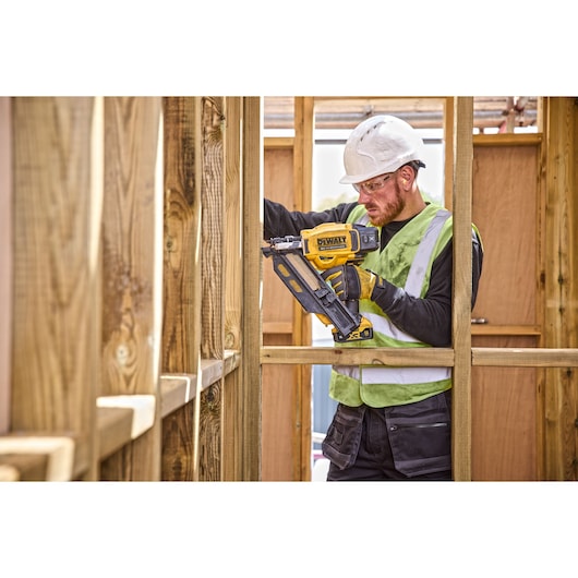 Worker uses a DEWALT cordless nailer DCN930N to build a wooden frame at a construction site.