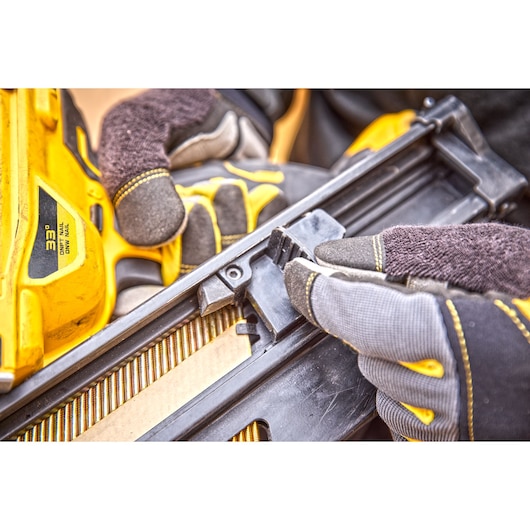 Gloved hands adjusting a DEWALT yellow nail gun magazine during setup at a worksite.