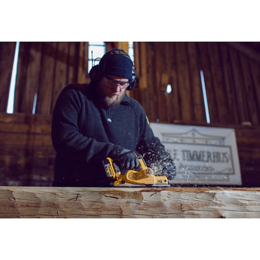 Person using a DEWALT DCP580P2 electric planer on a wooden beam in a workshop.