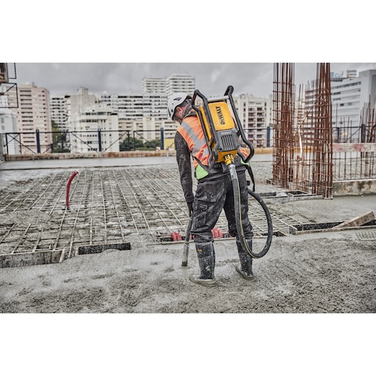 Worker uses DEWALT concrete tool on construction site, wearing safety gear and boots.