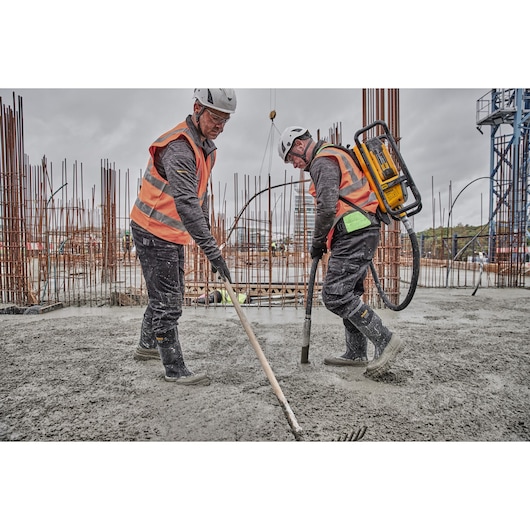 Two workers in safety gear use DEWALT equipment while working with concrete at a construction site.