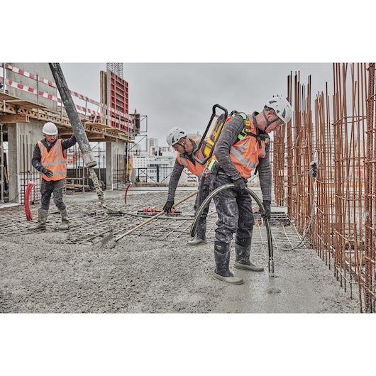 Construction workers in safety gear operate concrete equipment on a building site with rebar and wet cement.