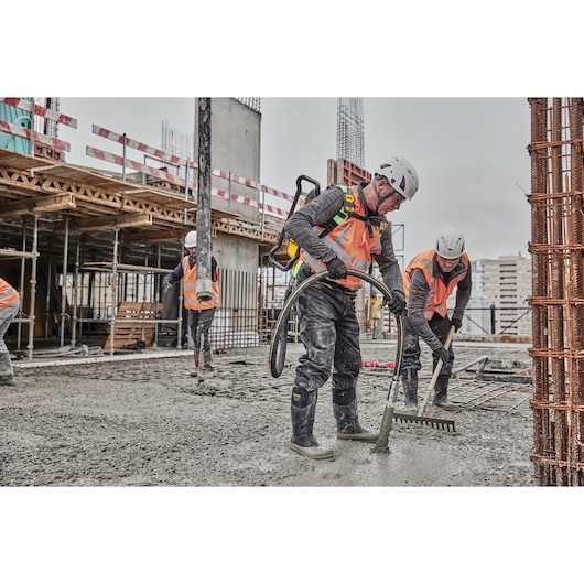 Workers in safety gear spread wet concrete at a construction site with tools and equipment.