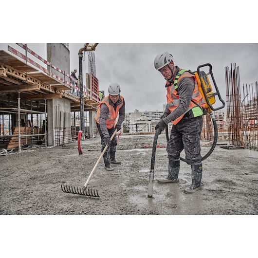 Two workers use DEWALT concrete tools on a construction site, wearing safety gear and helmets.