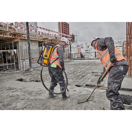 Two workers on a construction site use DEWALT tools to spread and level wet concrete for a building foundation.