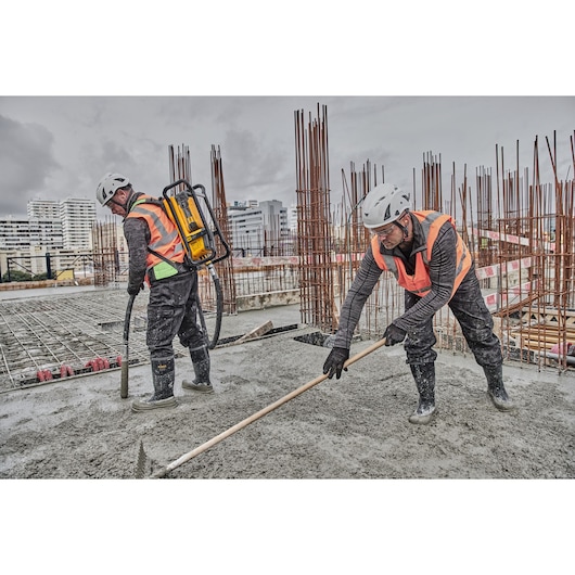 Two workers with helmets and vests use DEWALT equipment at a construction site, smoothing wet concrete.