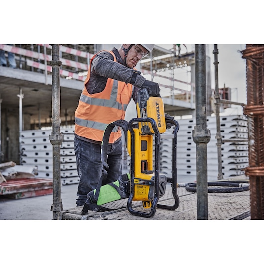 Worker uses a DEWALT DCPS310N tool at a construction site, wearing a safety vest and gloves.