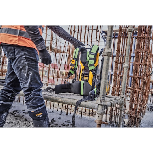 Worker on site with a DEWALT harness placed on a metal bench among construction rebar structures.