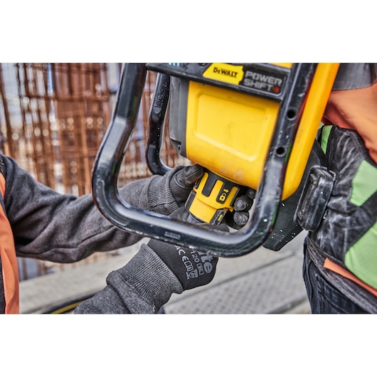 Worker wearing gloves handles a yellow DEWALT power tool on a construction site.