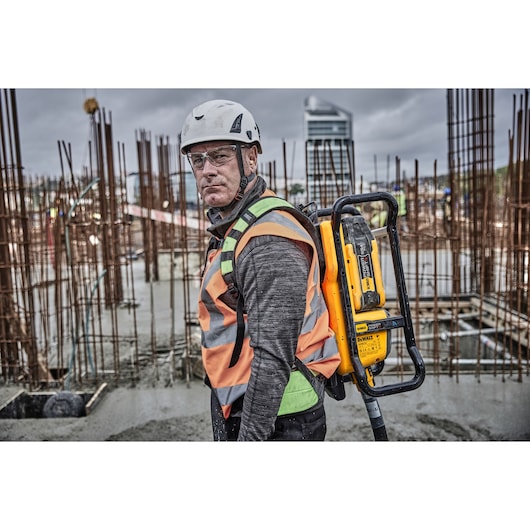 Worker wears a DEWALT DCPS310N tool backpack on a construction site with metal rods and concrete.