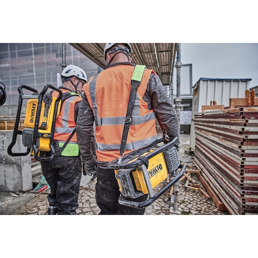 Two workers carry DEWALT tools and wear helmets and safety vests at a construction site.