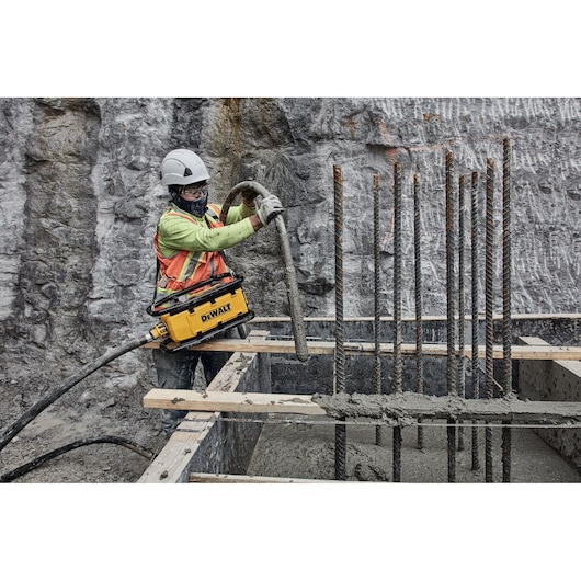 Worker using DEWALT tool for concrete work at construction site with rebar and safety gear.