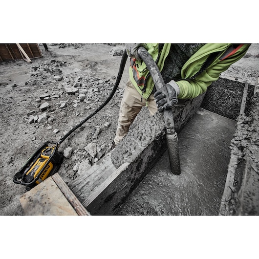 DEWALT concrete vibrator used by worker on construction site, smoothing wet concrete inside a wooden form.