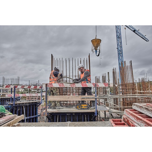 Two workers in safety gear at a construction site with steel rods and a DEWALT tool on a platform.