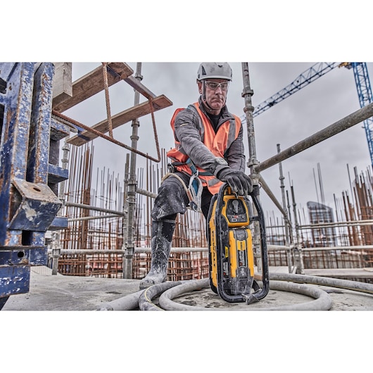 Worker uses a DEWALT DCPS320N tool at a construction site with scaffolding and safety gear.