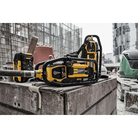 DEWALT Power Shift chainsaw and batteries on a construction site with building materials in the background.
