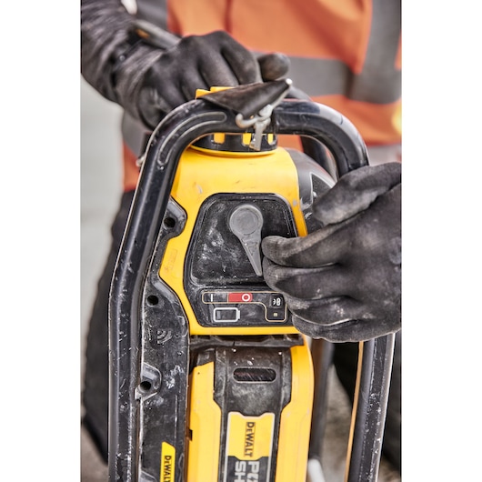 Close-up of DEWALT power tool being operated by a person wearing black gloves and a safety vest.