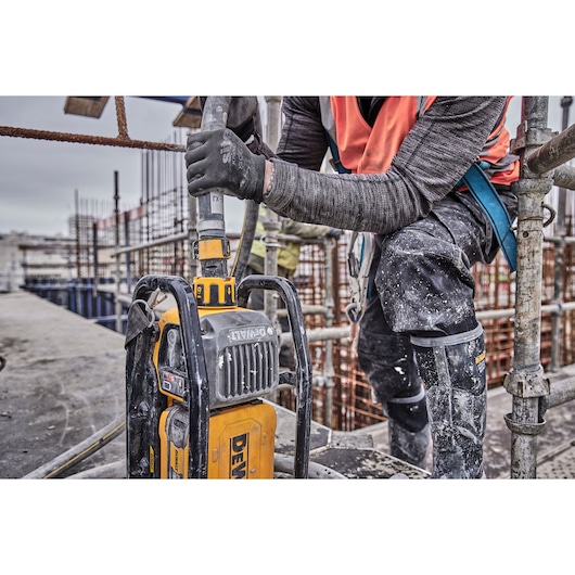 Worker using a DEWALT tool at a construction site, wearing gloves and safety gear. Concrete and metal rods visible.