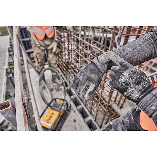 Worker wearing gloves operates DEWALT equipment at a construction site with metal rebar and safety gear visible.