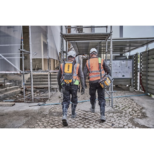 Two workers in safety gear and DEWALT equipment walking at a construction site.