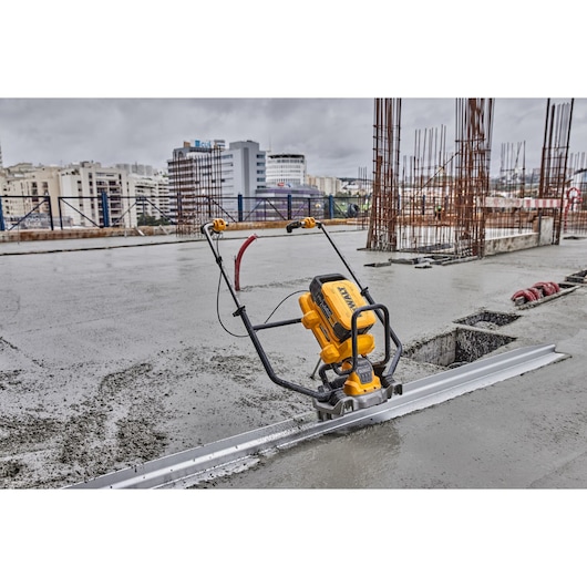 A DEWALT DCPS330N power tool used for smoothing concrete on a construction site, with buildings and metal rebar structures visible in the background.
