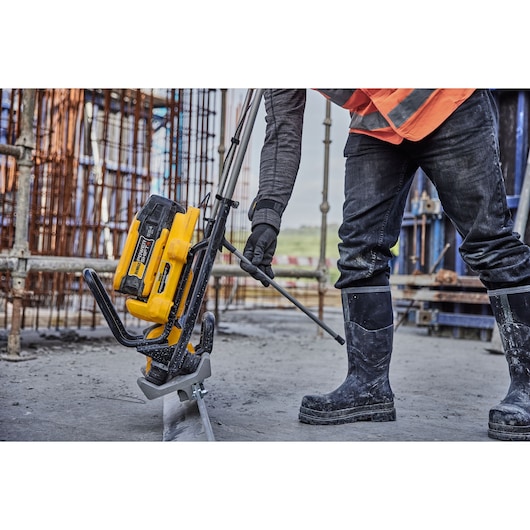 DEWALT tool in use at a construction site. Worker operates the device wearing boots and gloves.