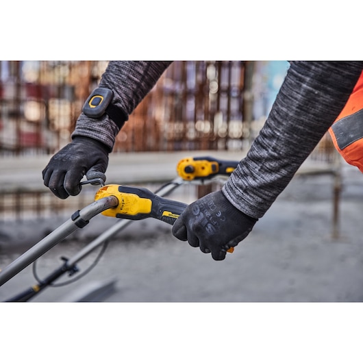 Worker adjusting yellow DEWALT power tool outdoors, wearing gloves and safety gear.