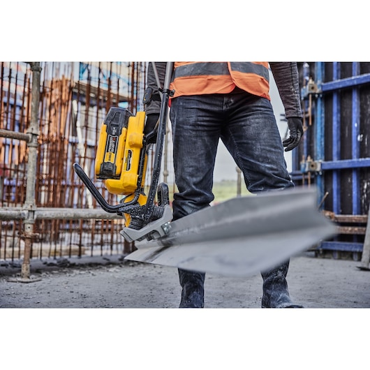 Worker uses DEWALT cordless metal shear tool to cut sheet metal at construction site, wearing safety gear.