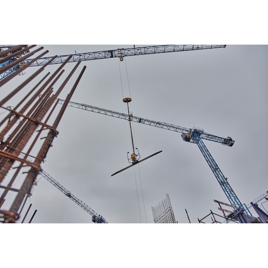 Construction cranes lift metal beams at a building site under a cloudy sky.