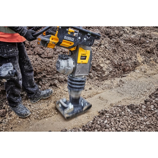 DEWALT compactor is being used on soil at a construction site by a worker wearing protective gear.
