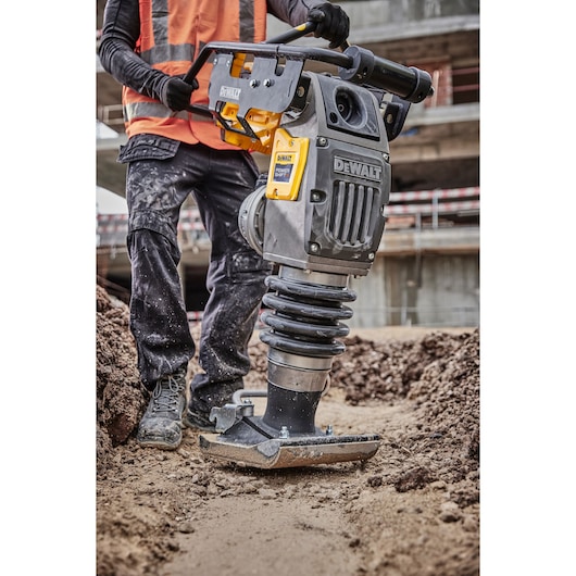 Worker uses a DEWALT DCPS660N power tool for compacting soil at a construction site.
