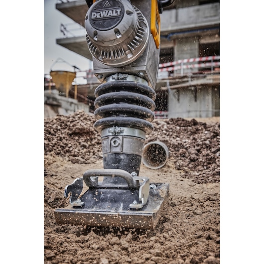 DEWALT compactor tamping soil at a construction site, machinery close-up with dirt flying.