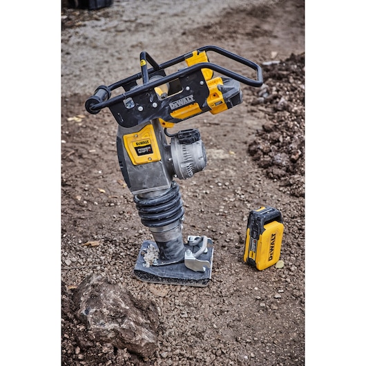 DEWALT cordless rammer tool on dirt, with detached battery beside it, used for soil compaction.