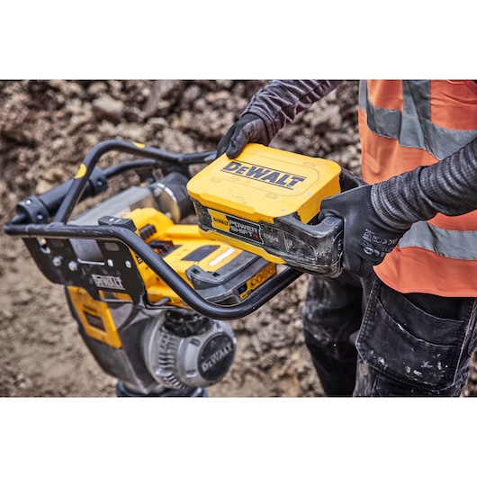 Person replacing DEWALT Power Shift battery in yellow equipment at construction site, wearing gloves and safety vest.