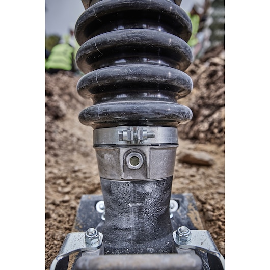 Close-up of a DEWALT power tool joint, showing metal clamp and spring, on a construction site with soil in background.