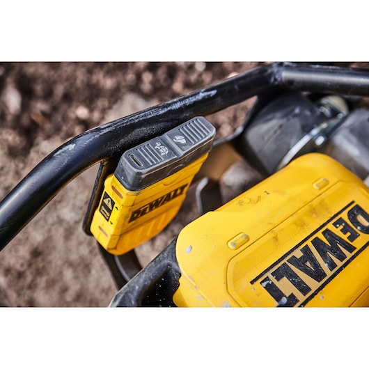 Close-up of a DEWALT battery attached to a yellow power tool outdoors.