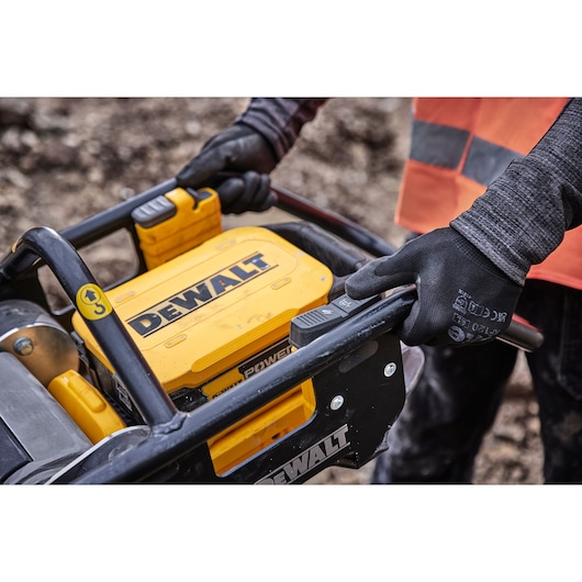 Worker uses DEWALT power tool outdoors, wearing gloves and safety vest.