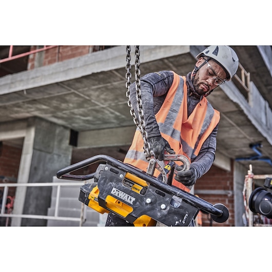 Worker in safety gear uses a DEWALT tool, DCPS660N, at a construction site with chains and concrete structure.