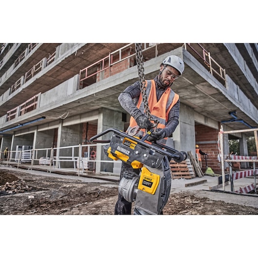 Worker at construction site holding a DEWALT chainsaw, wearing helmet and vest.