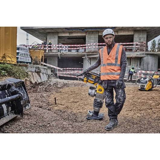 Worker with DEWALT DCPS660N tool at a construction site, wearing safety gear, surrounded by building equipment.