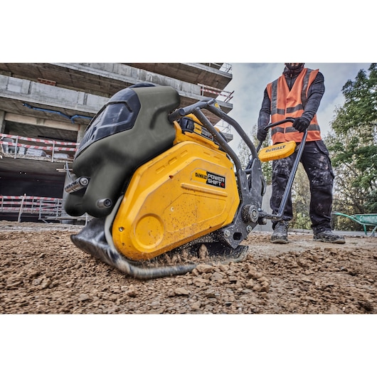 DEWALT Power Shift plate compactor in use on soil at a construction site by worker in orange vest.