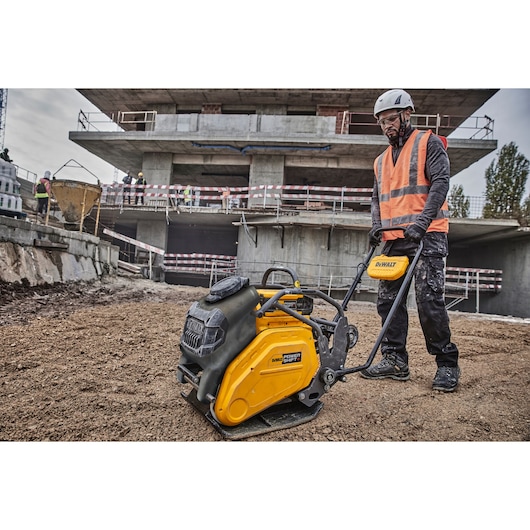 DEWALT plate compactor in use at a construction site, operated by a worker in safety gear.