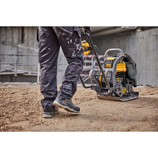 Person uses yellow DEWALT compactor on dirt at a construction site.