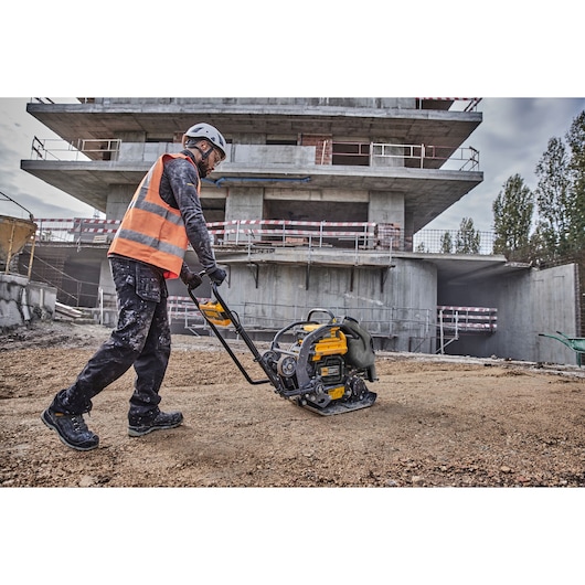 Worker uses DEWALT DCPS7154N plate compactor on construction site.