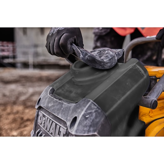 Gloved hand covers DEWALT equipment outdoors, close-up of protective cover being placed.