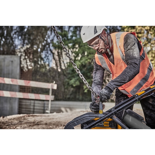 Worker in safety gear uses DEWALT DCPS7154N tool to attach chain at outdoor construction site.