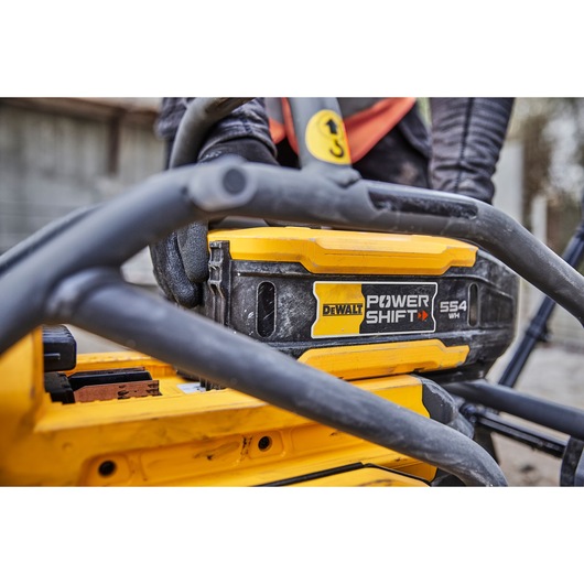 Close-up of a DEWALT Power Shift 554 WH battery installed in yellow power tool, with worker in the background.
