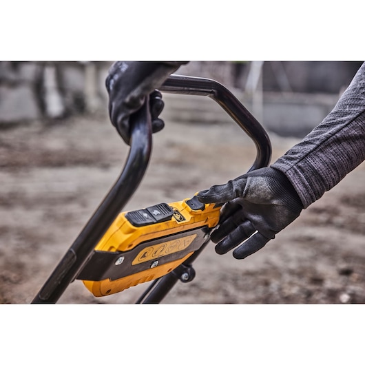 Person in gloves adjusts yellow DEWALT tool controls on handle outdoors.