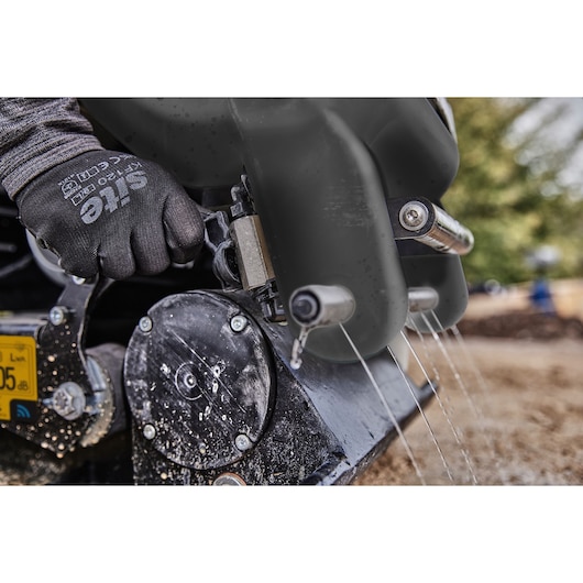 Close-up of a gloved hand adjusting a DEWALT machine with water spraying from its parts outdoors.
